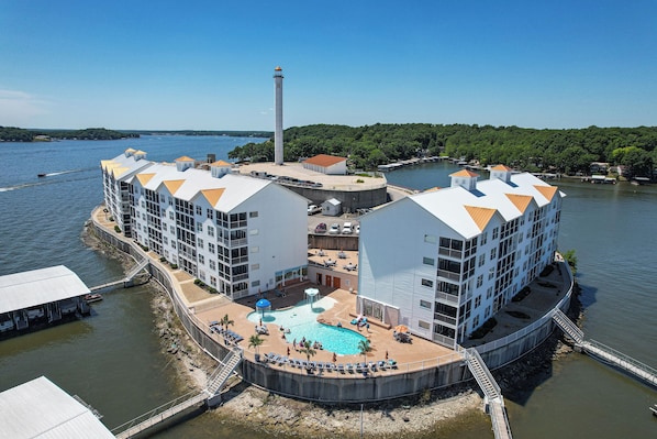 A waterfront hotel with multiple buildings, a swimming pool, and a lighthouse in the background.
