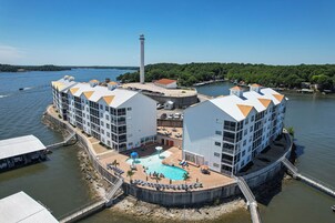Un hotel frente al mar con varias construcciones, una piscina y un faro al fondo.