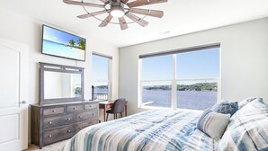 A bedroom with a large bed, a dresser, a desk, and a TV on the wall. - Island Life! Amazing Balcony-views-pool and Patio (Rocky Mount)