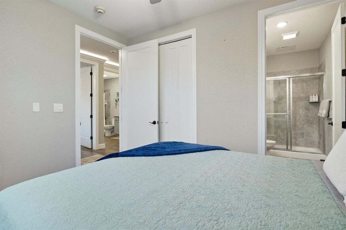 A bedroom with a bed, a bathroom with a shower, and a hallway leading to another room.