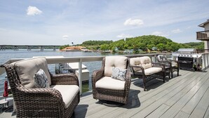 Eine Terrasse mit Korbmöbeln und einem Grill, mit Blick auf ein Gewässer und eine bewaldete Insel.