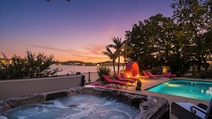 A hot tub and a pool with lounge chairs, set against a sunset view.