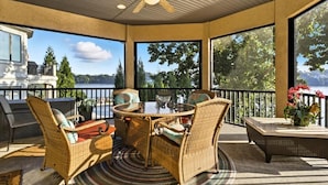 A covered patio with wicker furniture, a glass table, and a ceiling fan.