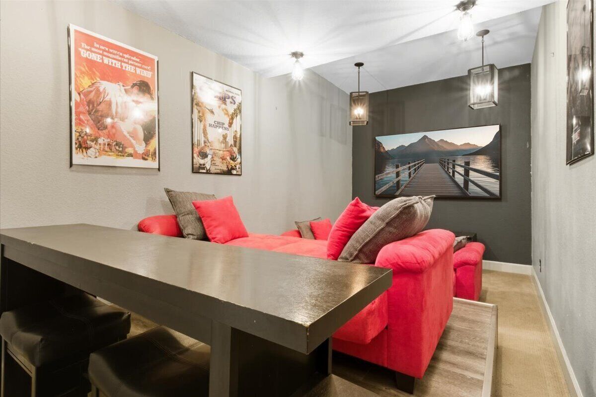 Una sala de estar moderna con un sofá rojo, una mesa de madera oscura y un cuadro grande con un paisaje de montaña.