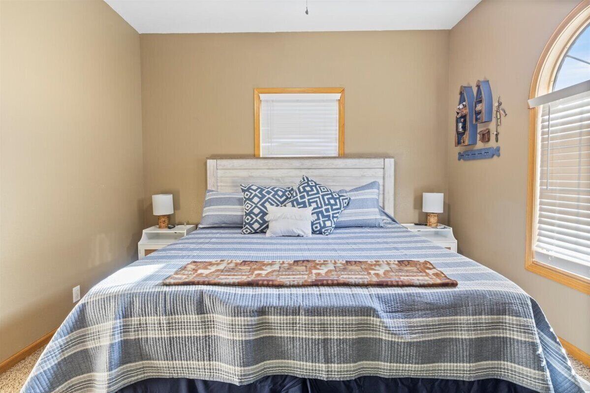 Une chambre à coucher comprenant un lit, deux tables de chevet, une fenêtre avec des stores et une étagère murale agrémentée d’objets décoratifs.