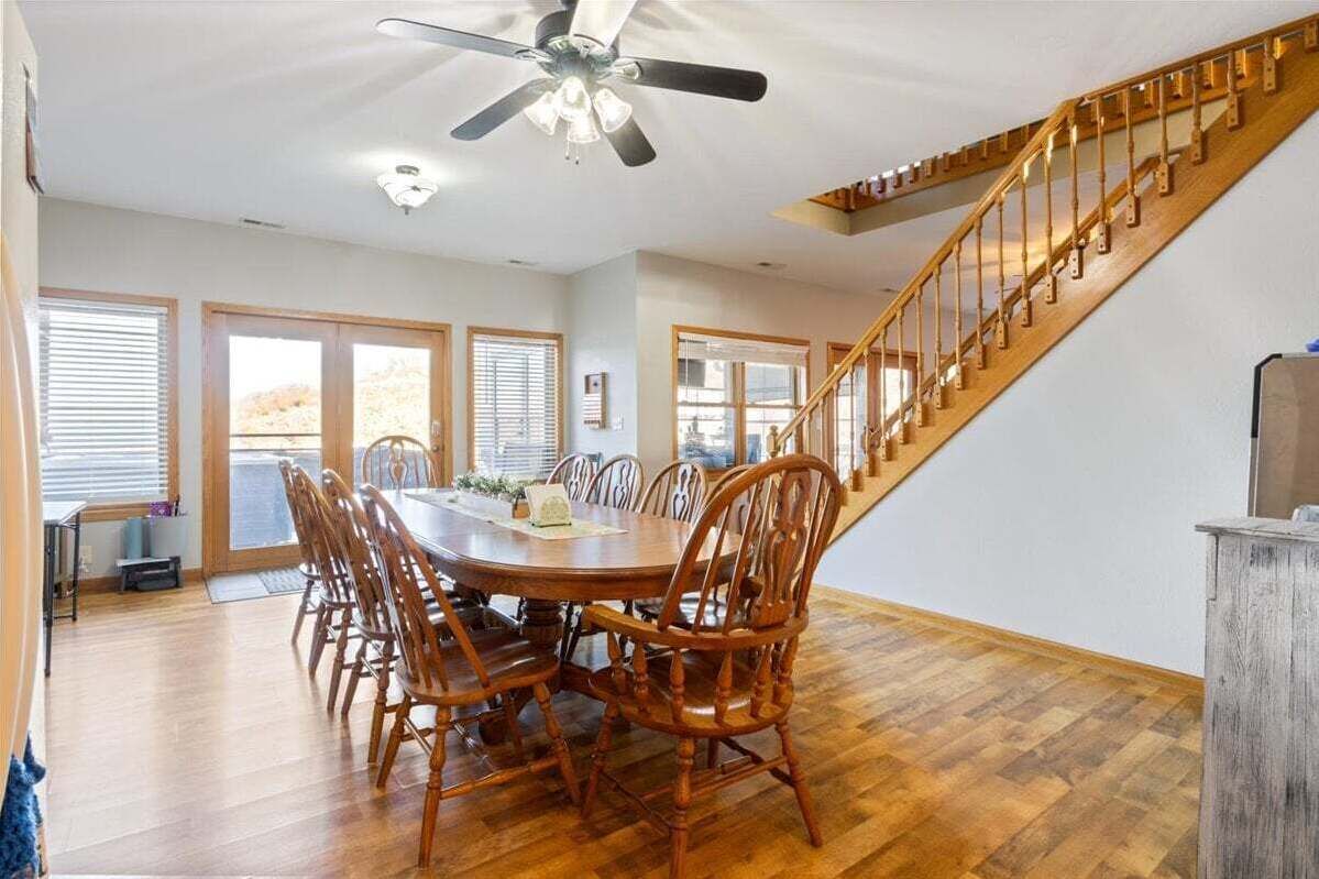 Een eetruimte met een houten tafel en stoelen, een plafondventilator en een houten trap.