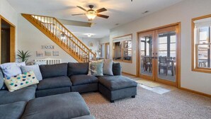 A spacious living room with a dark gray sectional sofa, a wooden staircase, and a ceiling fan.