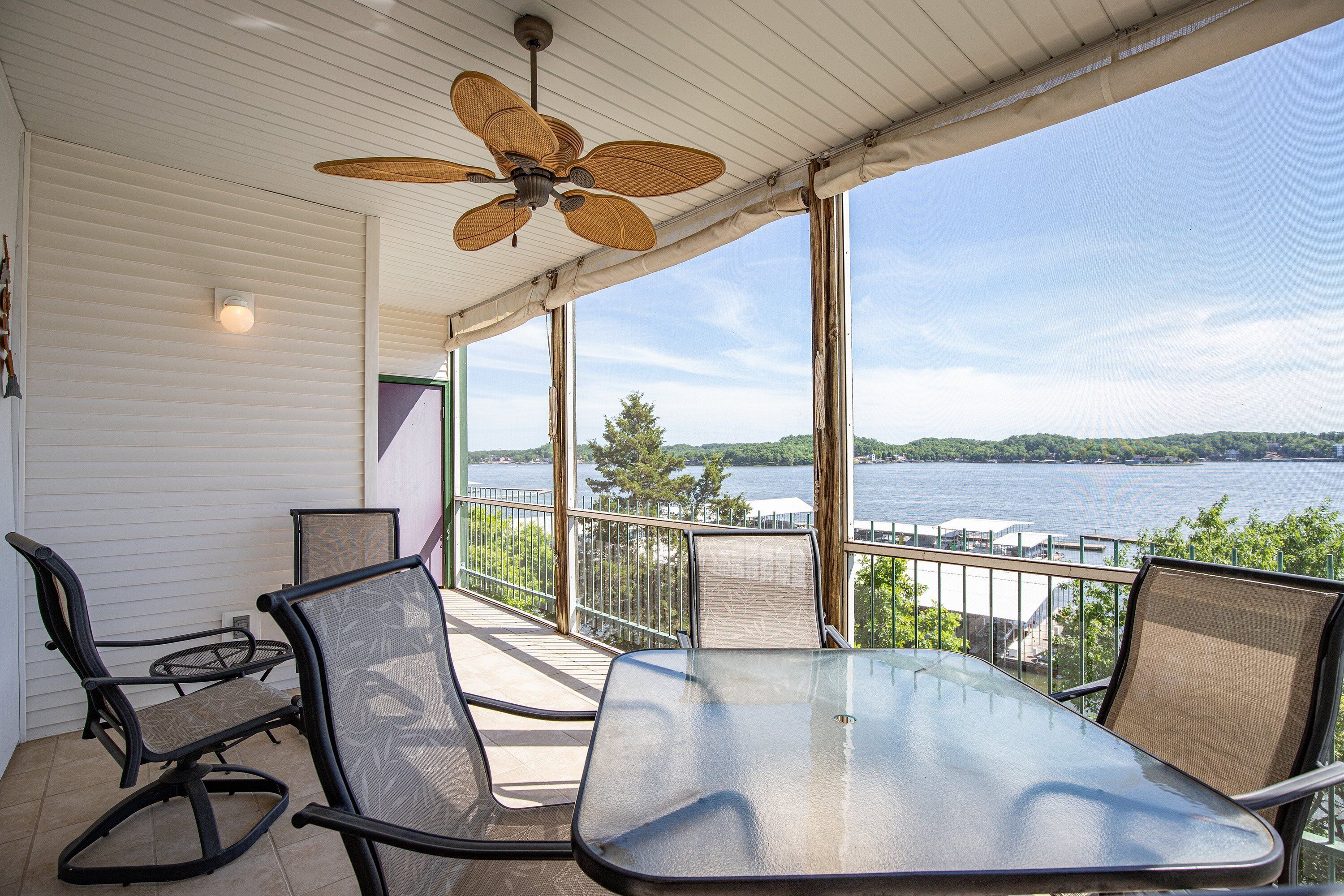 A balcony with a glass table and chairs, overlooking a lake.