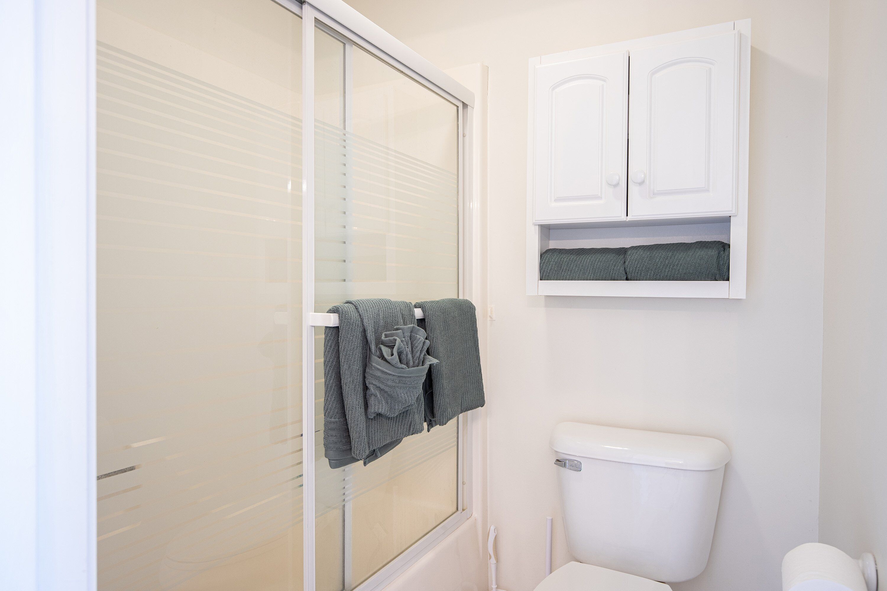 A bathroom with a toilet, a cabinet, and a towel rack with towels.