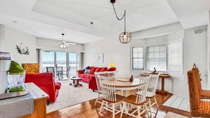 A spacious living area with a red sofa, white chairs, a wooden dining table, and a large window with blinds. - Breathtaking Views - Two Pools - Enclosed Balcony (Lake Ozark)
