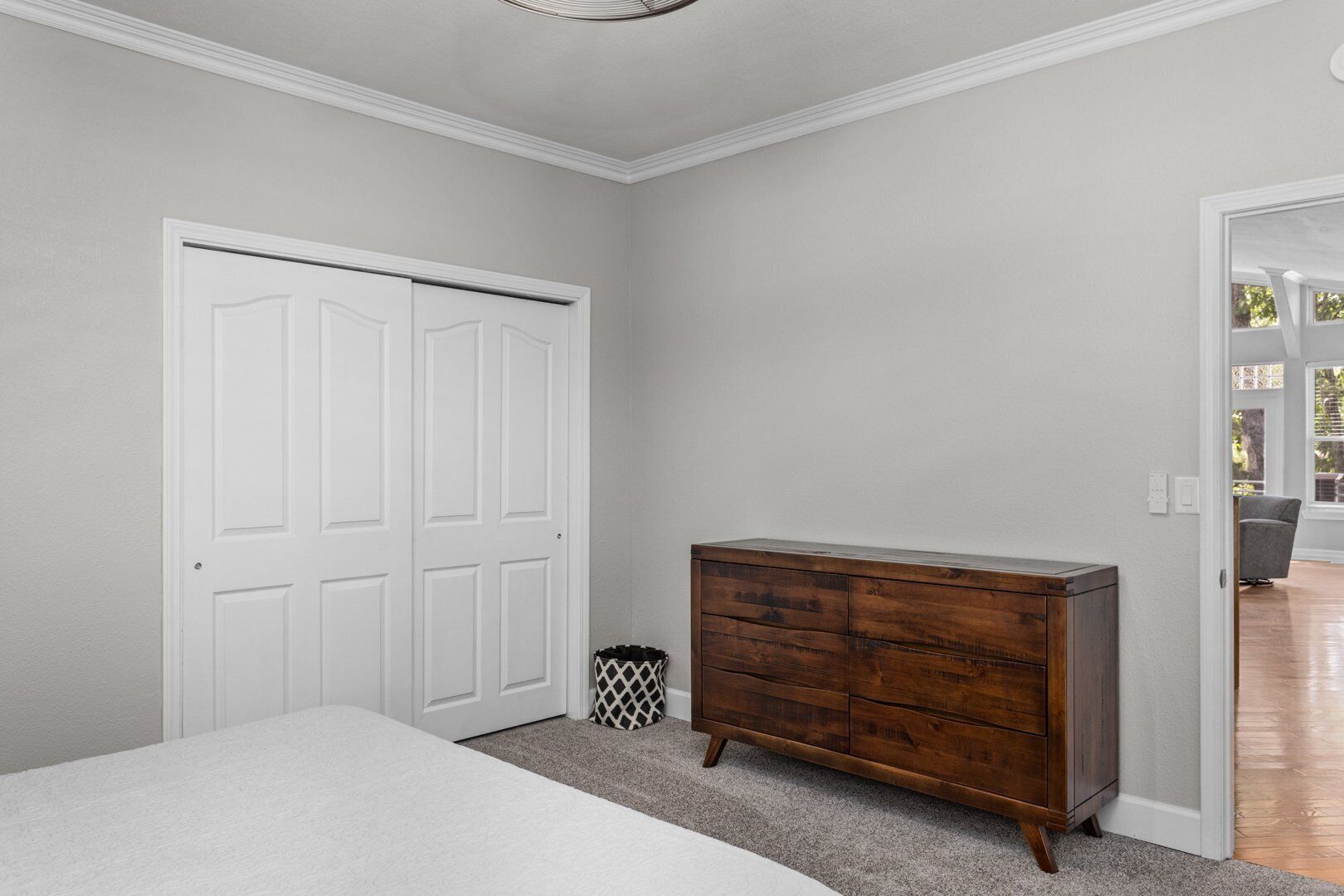 A bedroom with a white bed, a wooden dresser, and a white door.