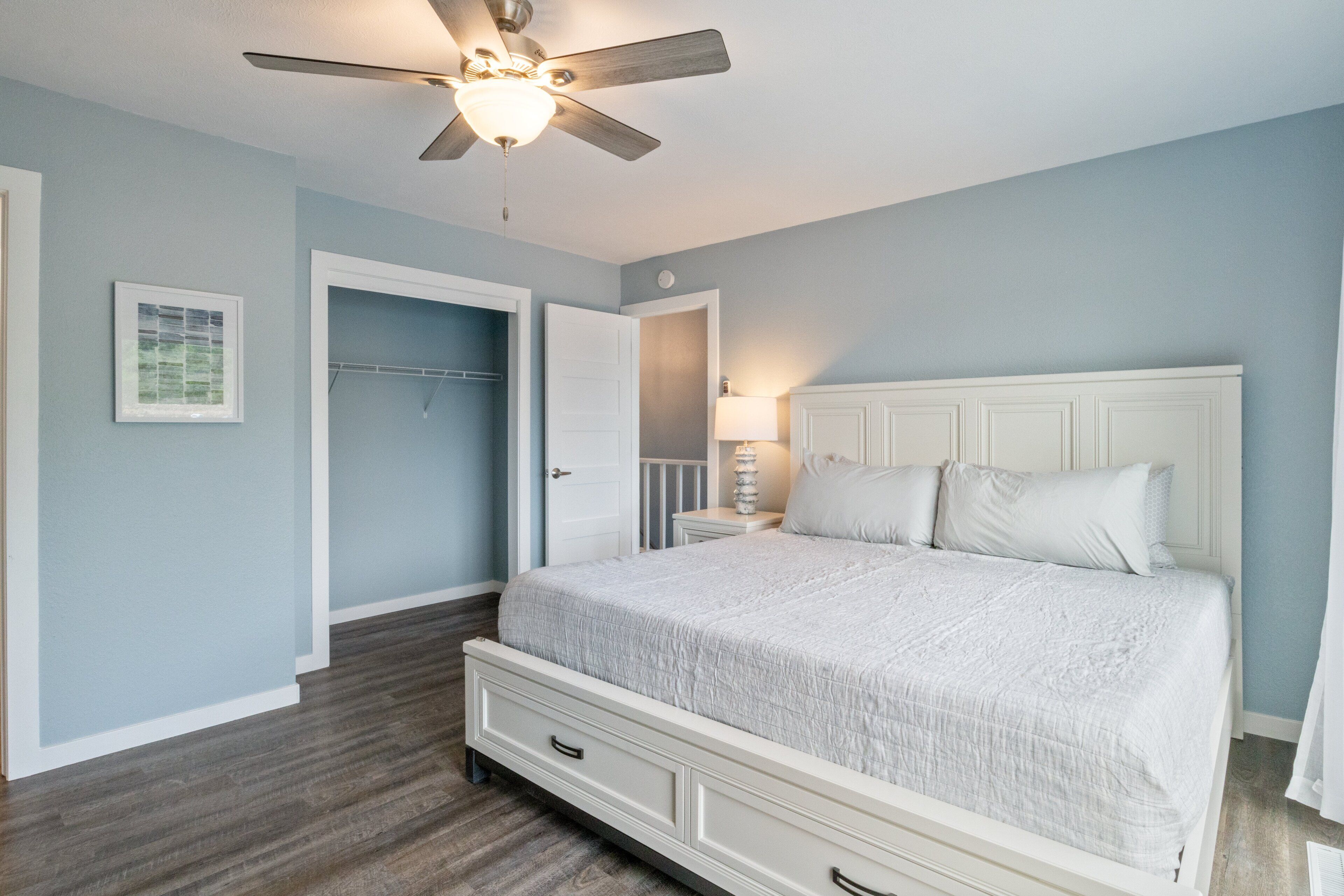 A bedroom with a bed, a ceiling fan, a nightstand, and a door.