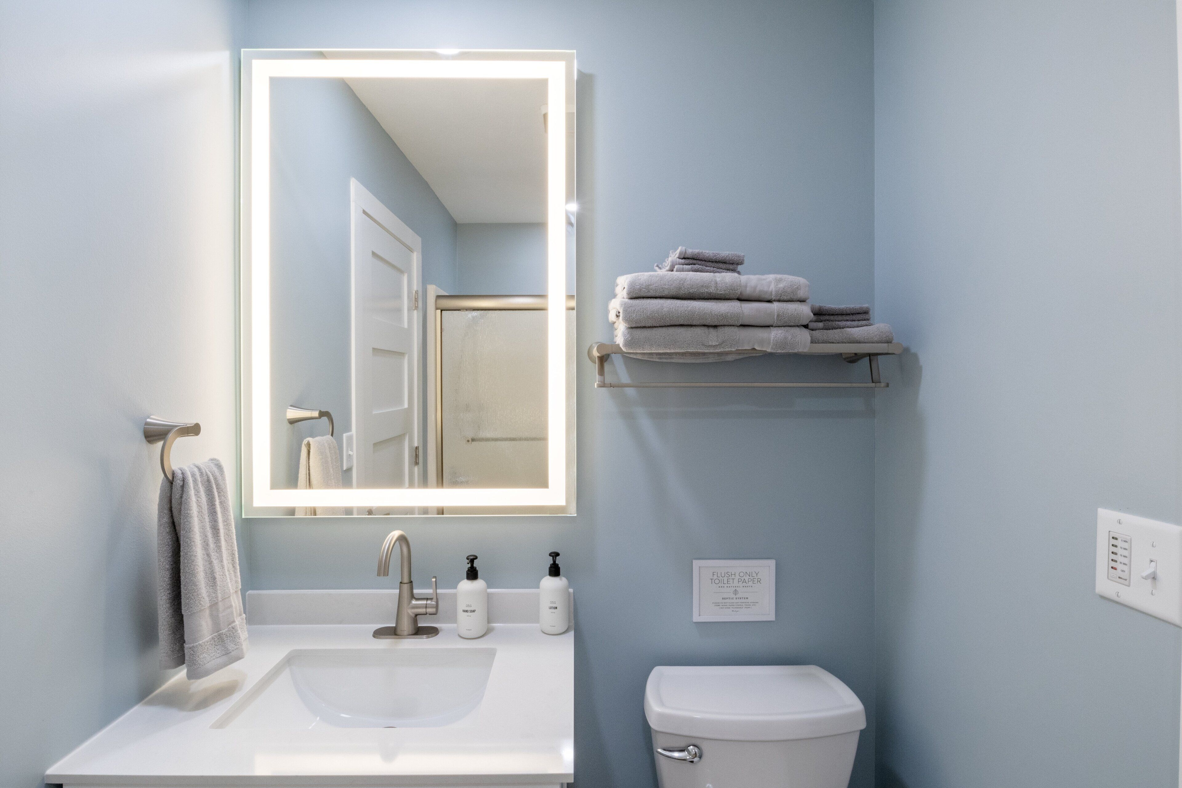 A bathroom with a sink, mirror, towel rack, toilet, and a shelf with folded towels.