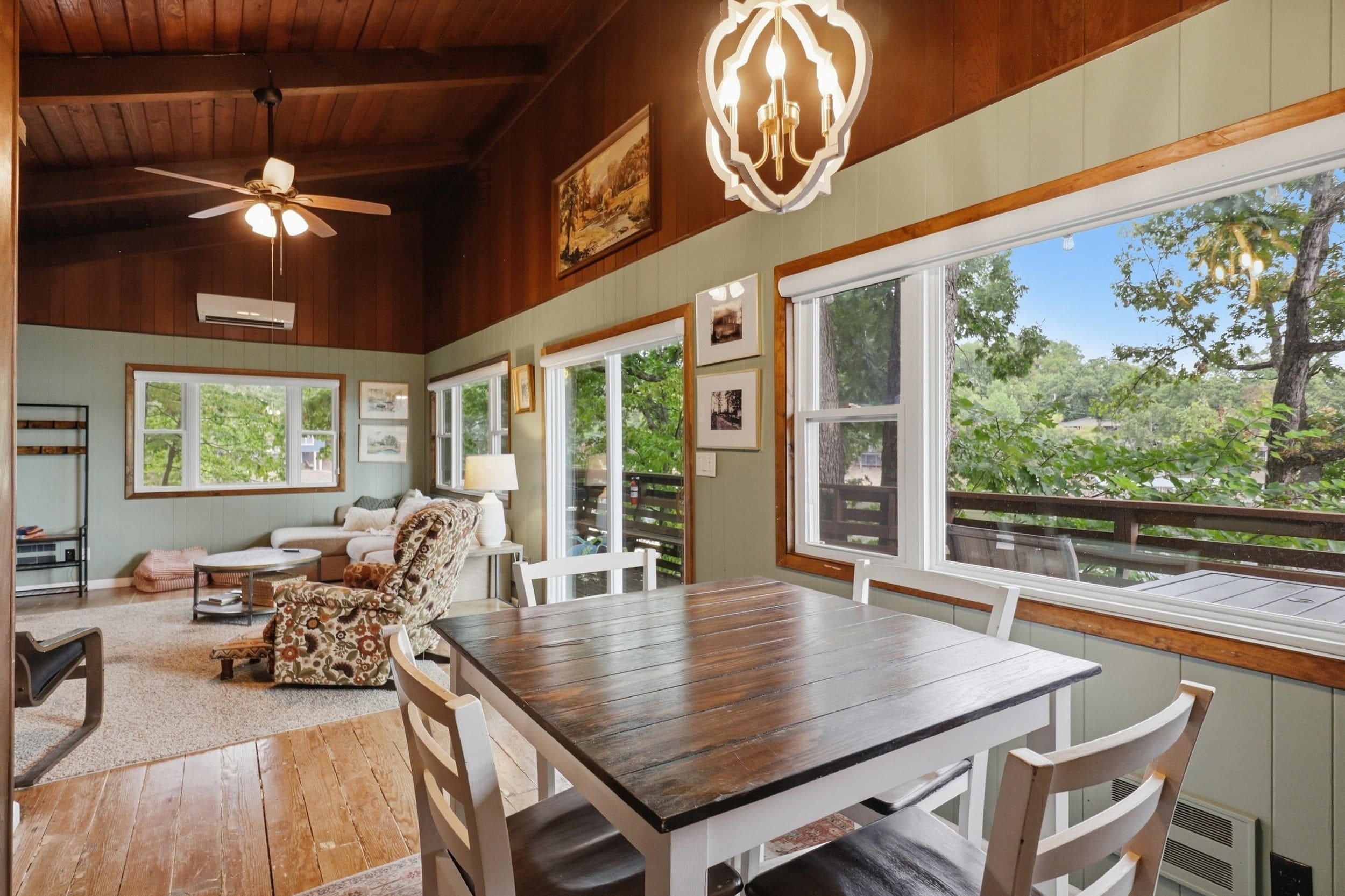 Un comedor amplio con una mesa y sillas de madera, ventanas grandes que ofrecen vistas al exterior y un ventilador de techo.