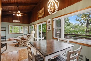 Un comedor amplio con una mesa y sillas de madera, ventanas grandes que ofrecen vistas al exterior y un ventilador de techo.
