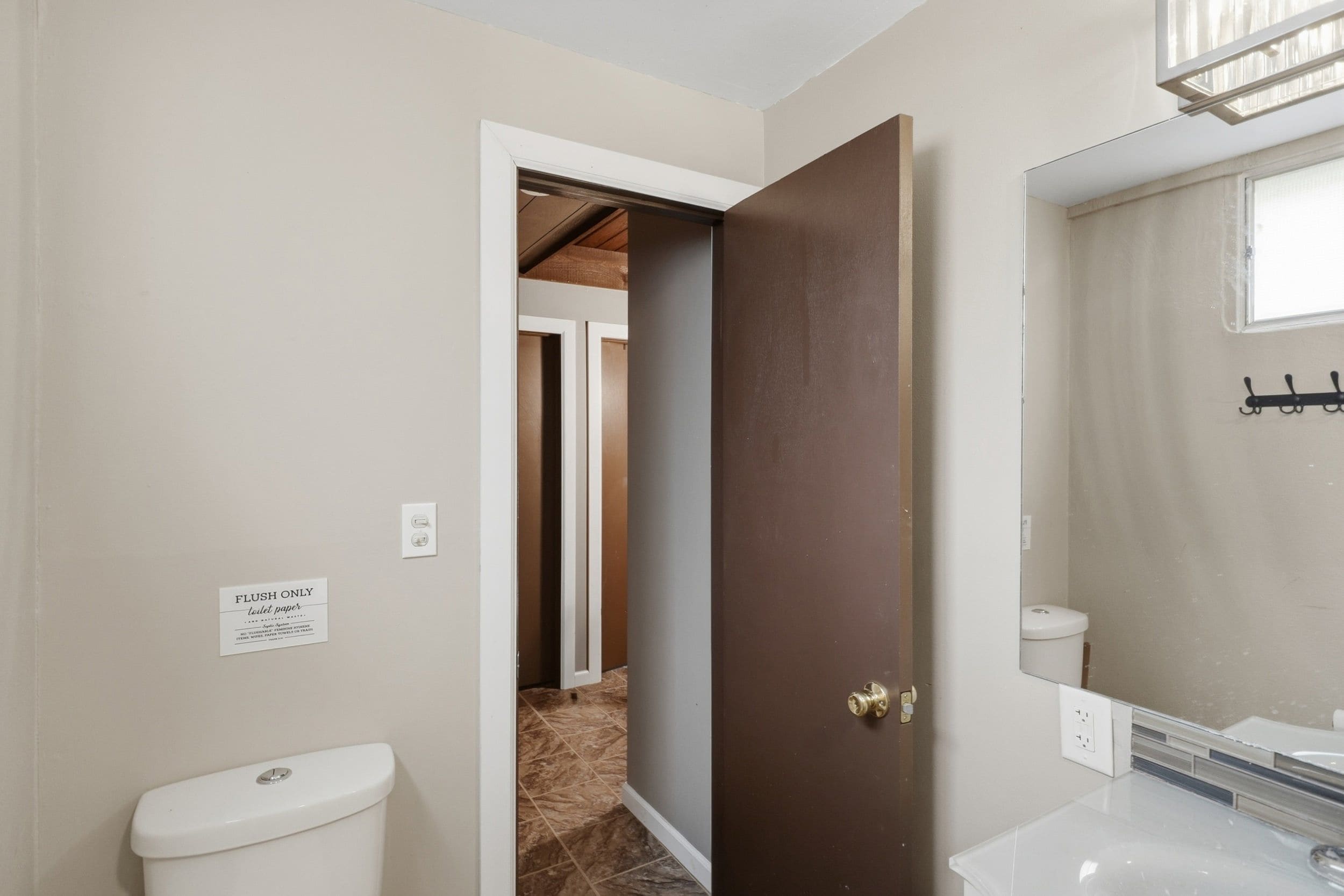 Un bagno con il water, un lavandino e uno specchio. Una porta dà accesso a un'altra stanza.