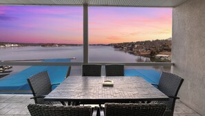 A terrace with a table and chairs overlooking a body of water and a cityscape during sunset. - Nautical-inspired Lakefront Unit w/ Awesome Views (Osage Beach)