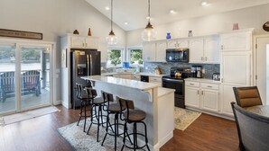 A modern kitchen with white cabinetry, a large island with bar stools, and a view of the outdoors. - Incredible Views, Spacious Deck, Private Dock, Gas Grill, Games & Cards (Gravois Mills)