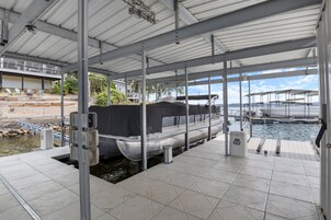 Un muelle techado con techo de metal, un bote cubierto con un toldo negro, y vista al agua y embarcaciones amarradas.