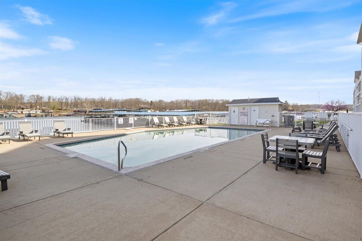 A rooftop pool area with lounge chairs and tables, surrounded by a white fence.