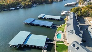 An aerial view of a lakeside property with docked boats, a swimming pool, and a large building with a sloped roof. - Newly Updated, Amazing Views, Boat Slip & Heated Pool (Sunrise Beach)