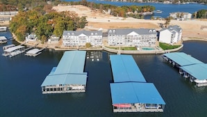 A waterfront hotel with multiple docked boats, a large building with a blue roof, and a scenic view of a lake and forest. - Newly Updated, Amazing Views, Boat Slip & Heated Pool (Sunrise Beach)
