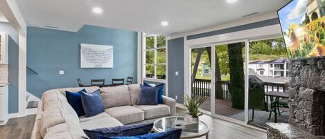 A modern living room with a beige sectional sofa, a glass coffee table, and a view of the outdoor patio area.