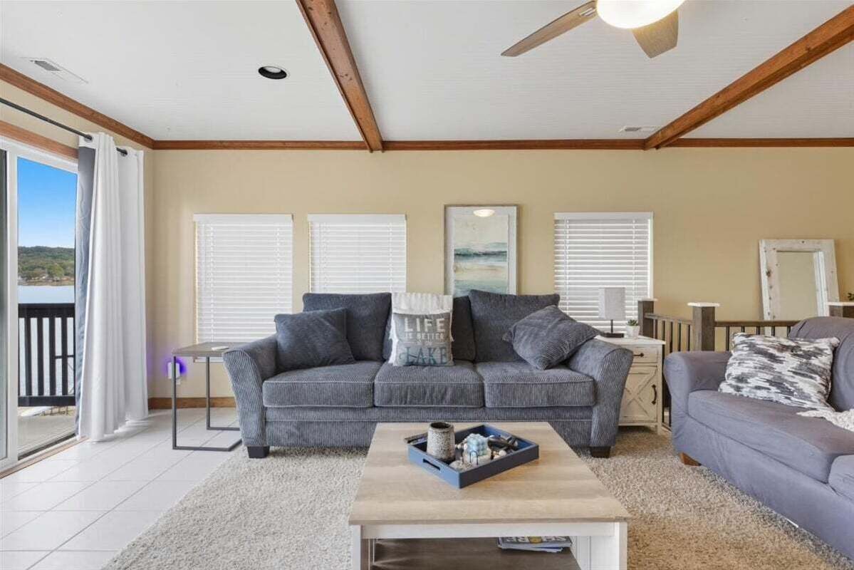 A living room with a grey sofa, a coffee table with decorative items, and a balcony with white curtains.