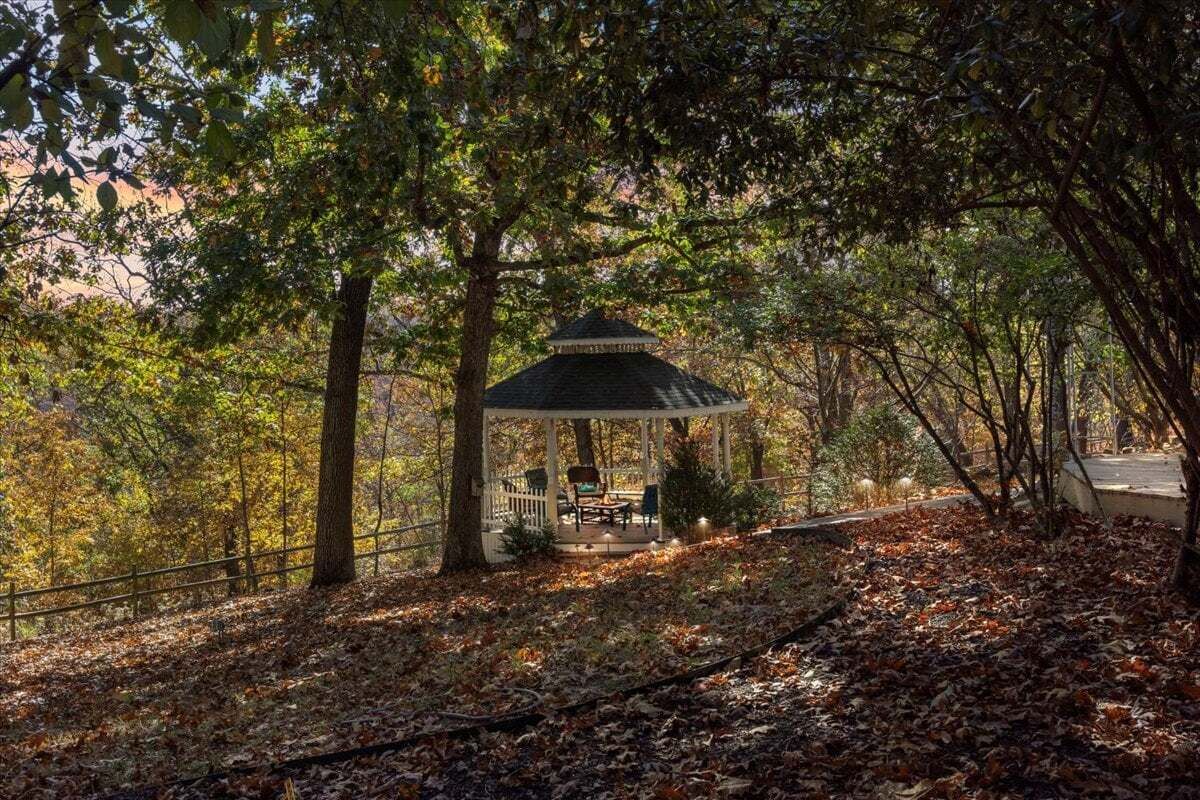 A gazebo with a roof and seating area surrounded by trees and fallen leaves.