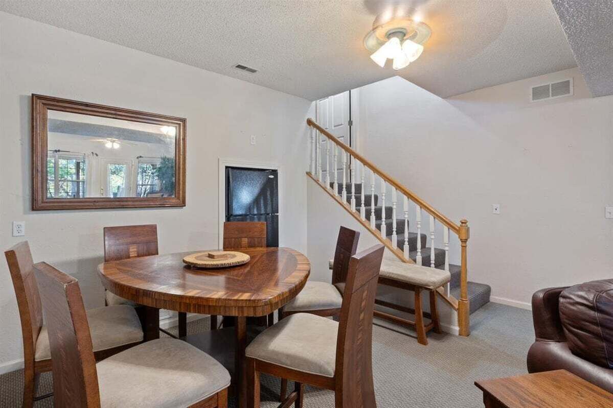 A dining area with a round wooden table and chairs, a large mirror, and a staircase with wooden railings.