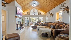 Ein großzügiges Wohnzimmer mit hoher Holzbalkendecke, Kamin und großem Fenster.
