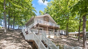 A two-story house with a stone facade, a balcony, and a wooden deck. - Stunning Views of the 7.5mm, Private Dock, Spacious Decks, Kayaks & More! (Gravois Mills)