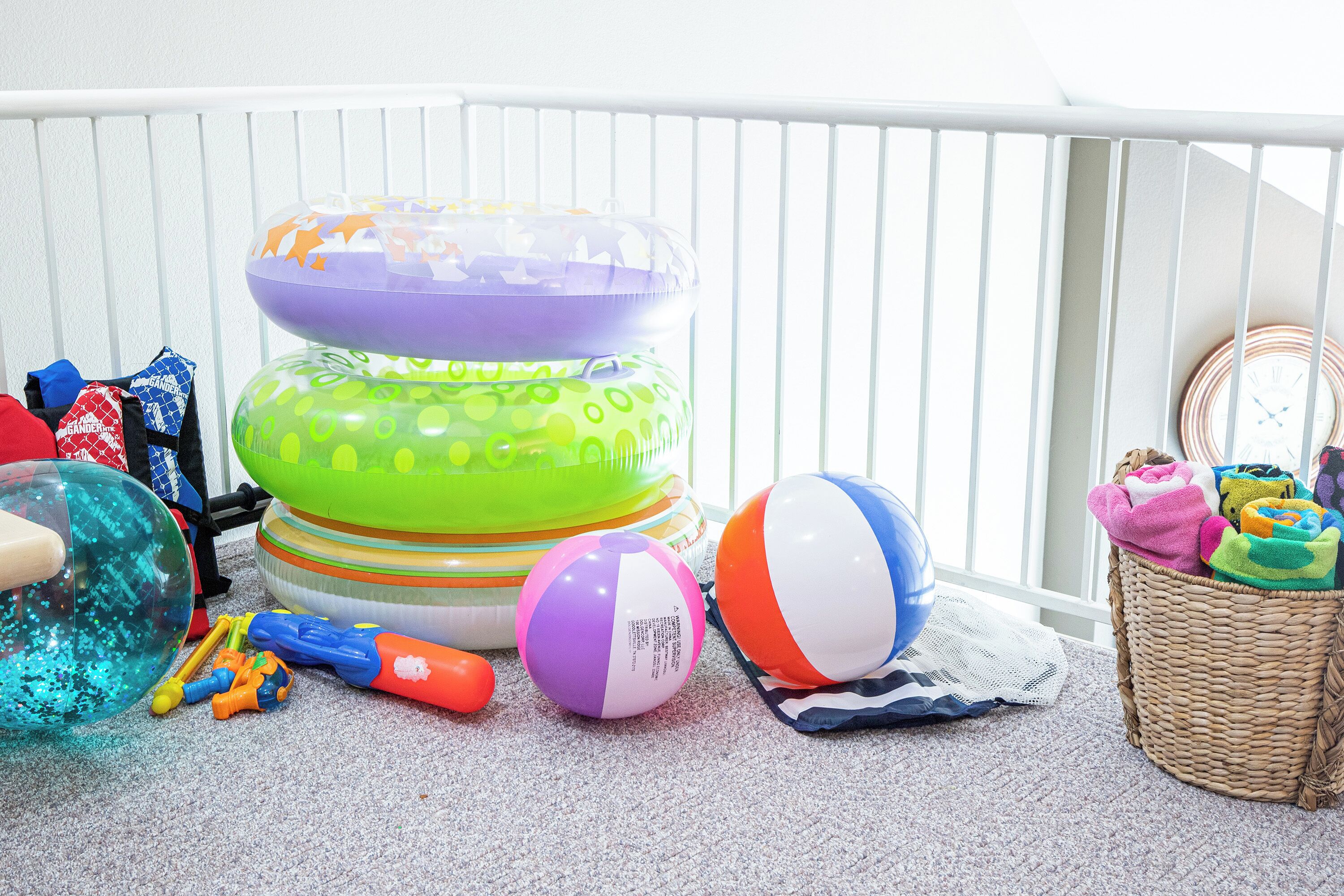 A room with a white crib, a stack of colorful inflatable toys, a beach ball, and a wicker basket with towels.