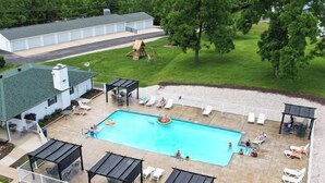 Une piscine entourée d’une terrasse délimitée par une clôture, avec des chaises longues et des parasols.
