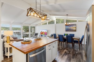 Una cocina moderna con una isla de madera, electrodomésticos de acero inoxidable y una zona de comedor con sillas azules y una mesa.