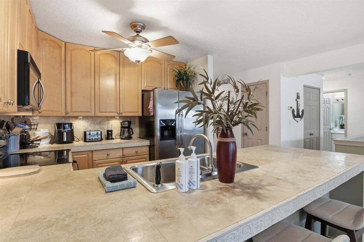 A kitchen with wooden cabinets, a stainless steel refrigerator, a coffee maker, a toaster, and a plant on the counter.