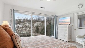 Une chambre à coucher avec un grand lit, une commode, un téléviseur et une vue sur l’extérieur.
