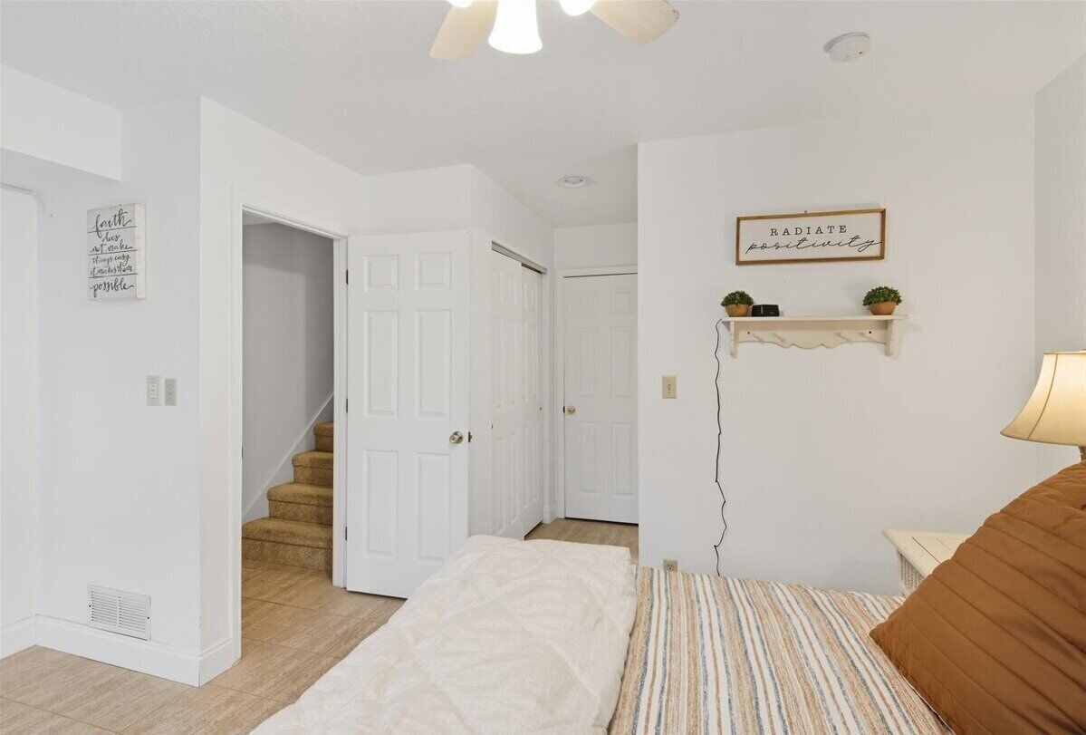 Un dormitorio con cama, mesita de noche, estante en la pared con plantas y una puerta que da a otra habitación.