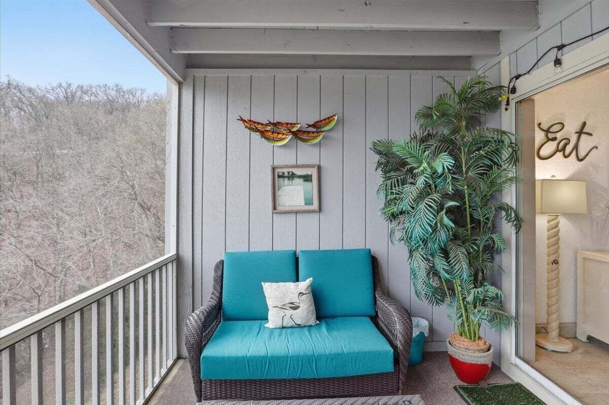 Un balcone con un divano in vimini, una pianta in vaso e un quadro appeso al muro.