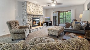 A living room with a stone fireplace, a ceiling fan, and a large window offering a view of the outdoors. - Lazydays Pet-friendly Condo w/ Pool & Slip at 3M (Osage Beach)