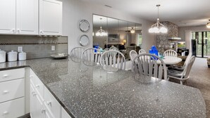 A modern kitchen with granite countertops, white cabinetry, and a dining area with white chairs. - Lazydays Pet-friendly Condo w/ Pool & Slip at 3M (Osage Beach)