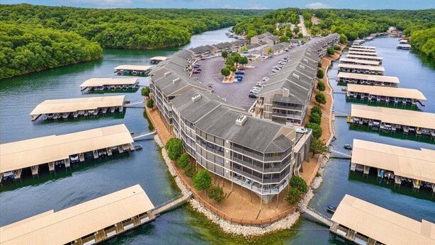 A riverside hotel with multiple floating structures connected by walkways, surrounded by lush greenery. - Lazydays Pet-friendly Condo w/ Pool & Slip at 3M (Osage Beach)