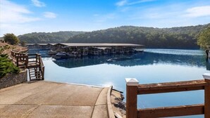 A lakeside view with a dock, wooden deck, and a covered area with boats. - Lazydays Pet-friendly Condo w/ Pool & Slip at 3M (Osage Beach)