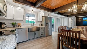 A modern kitchen with stainless steel appliances, a granite countertop, and a dining area with wooden chairs and a table. - Amazing Lakefront Paradise With Perfect Location (Osage Beach)