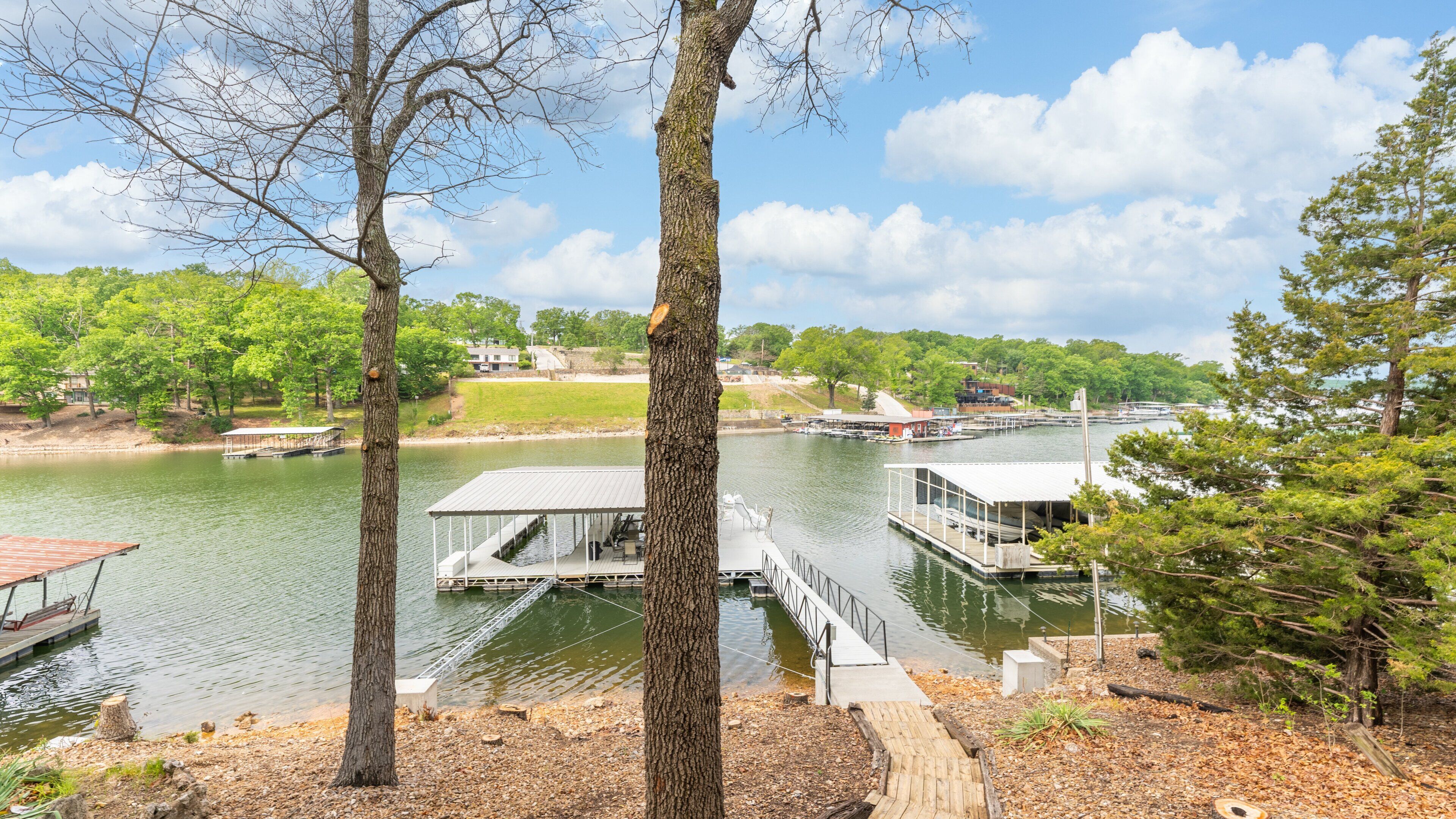 A lakeside dock with a covered seating area, a boat, and a small building.