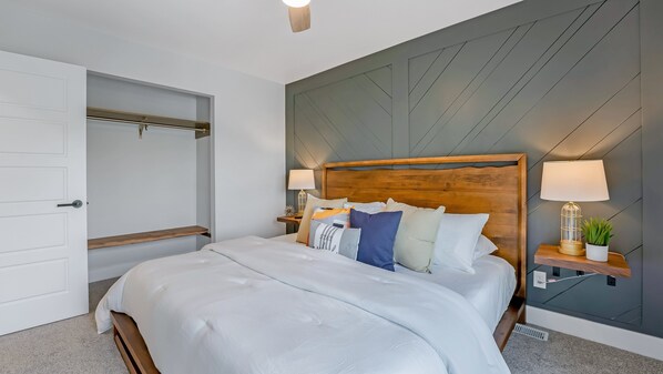 A neatly made bed with a wooden headboard, a bedside table with a lamp, and a small plant. - Amazing Lakefront Paradise With Perfect Location (Osage Beach)