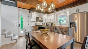 A modern kitchen with white cabinets, stainless steel appliances, and a wooden dining table. - Amazing Lakefront Paradise With Perfect Location (Osage Beach)
