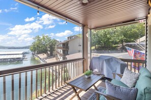 A balcony with a view of a lake, a covered grill, and a seating area with a cushion. - Lakefront Couple Retreat Near Hot Spots and Dining (Lake Ozark)