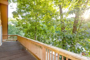 A wooden balcony with a metal floor, overlooking a lush green area with trees and a building in the background. - Quiet Cove, Lake Views, Grill, Private Dock (Sunrise Beach)