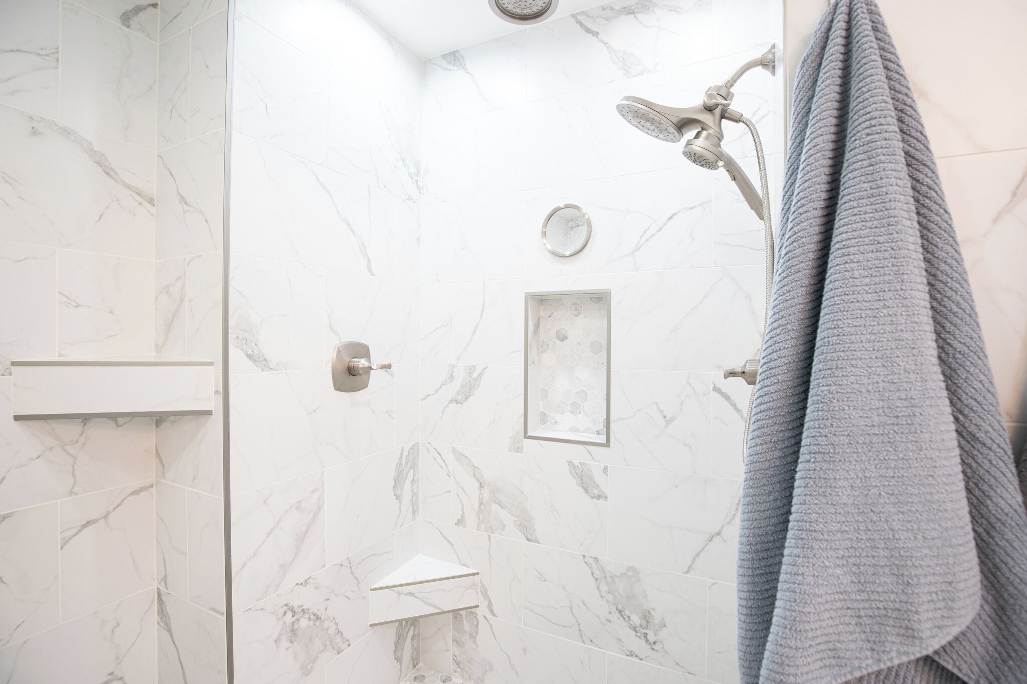 A bathroom with marble walls, a shower, and a towel rack.